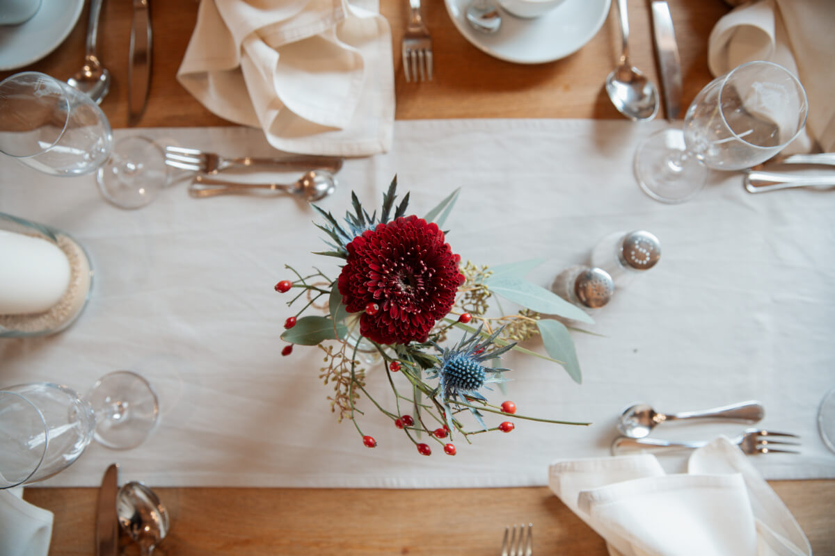 Einfache Tischdekoration, Glasvase mit bordeauxfarbener Gerbera und Beeren